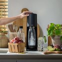 Zwarte SodaStream Terra met bruisende fles, glas met limoen, mandje pruimen en fruit.