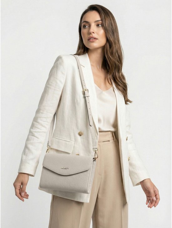 Lichtgrijze lederen schoudertas met goudkleurig logo, gedragen door een model met een witte blazer.
