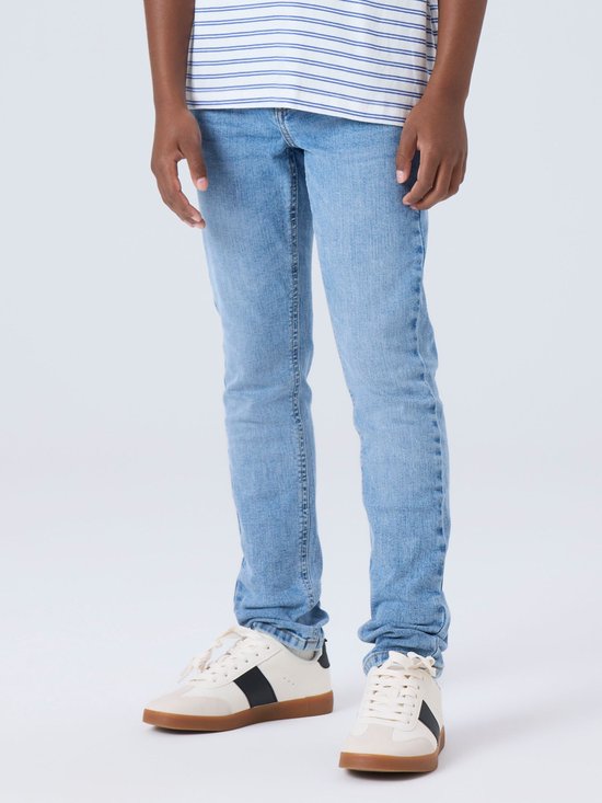 Onderlichaam van een jongen in een lichtblauwe spijkerbroek en witte sneakers.