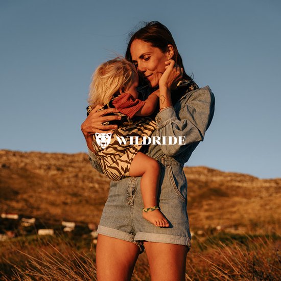 Vrouw in spijkeroutfit knuffelt kind dat in draagzak met bruine zebraprint zit.