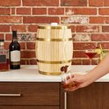 Houten vat met tapkraan, met een hand die een glas vult, bij een bakstenen muur.