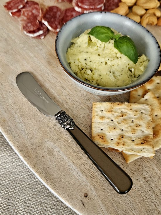 Een bruin botermesje met parelmoer handvat en gedetailleerd zilverkleurig ornament op een houten plank met crackers en dips.