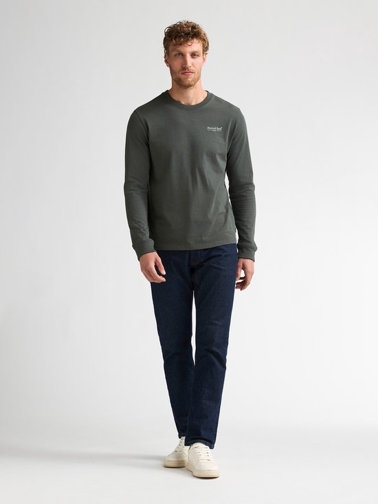 Man met donkergroene longsleeve, donkere jeans en witte sneakers.