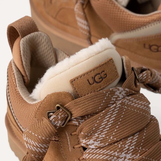 Close-up van een bruine UGG sneaker met witte wolvoering en een veter met sneeuwvlokkenpatroon.