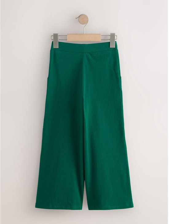Groene wijde broek van tricotstof met steekzakken, hangend aan een kledinghanger.