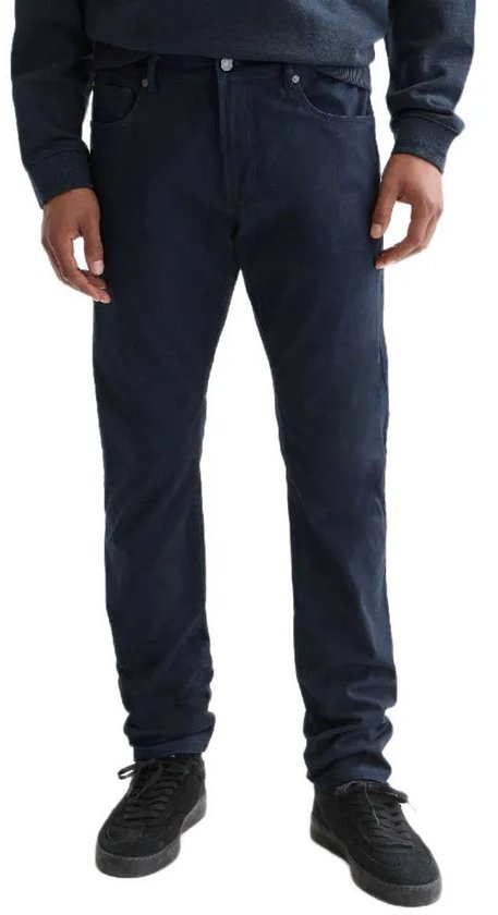 Een man van voren gezien in een donkerblauwe broek met vijf zakken en zwarte sneakers.