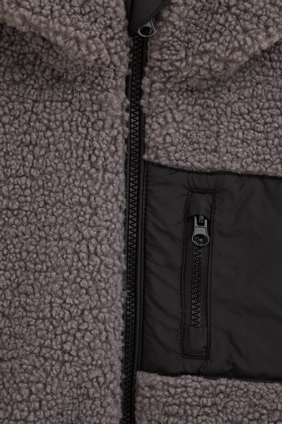 Sluiting van een grijze teddy jas met een zwart nylon borstvakje met rits.