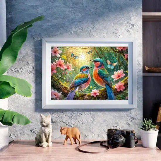 Een ingelijst puzzel van 500 stukjes, "Greeting the New Day", met twee kleurrijke vogels op een tak, bloemen en vlinders, hangend aan een muur.