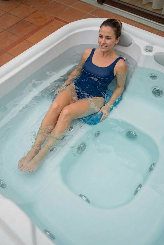 Vrouw met een donkerblauwe badpak in een bubbelbad, zittend op een blauw spa zitkussen.