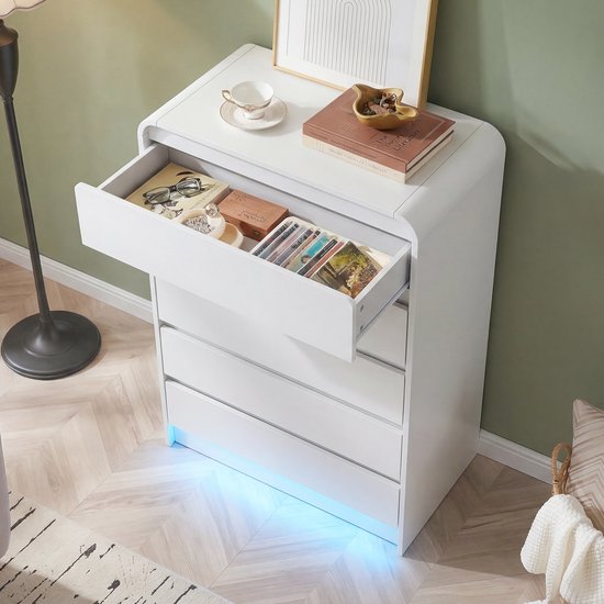 Strakke witte ladekast met 5 laden, een open lade toont diverse spullen. De kast heeft afgeronde hoeken en subtiele blauwe LED-verlichting aan de onderkant.