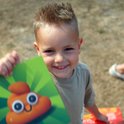 Jongen met bruin haar lacht, houdt kaart met bruine drol met ogen vast.
