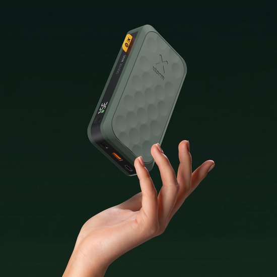 Groene Xtorm powerbank met honingraatmotief, digitale weergave en gele aan/uit-knop, zwevend boven een hand.