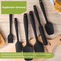Diverse zwarte siliconen spatels en een bakkwast liggen op een houten tafel.