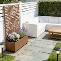 Bruin tuinscherm met plantenbak met lavendel en hortensia's, naast een witte hoekbank.