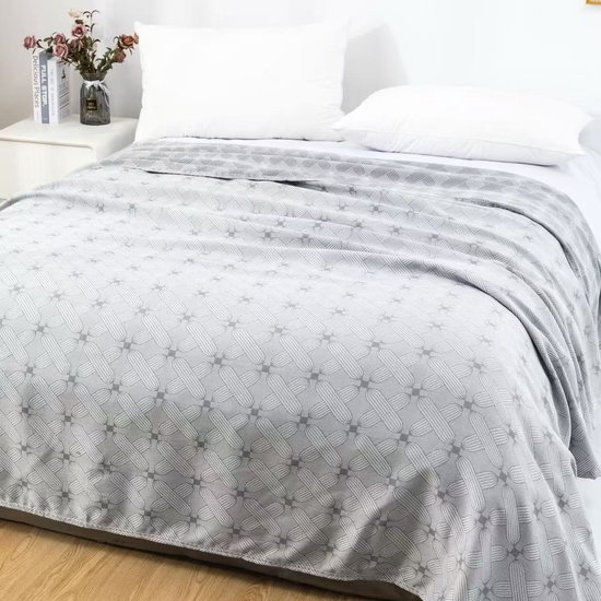 Grijze deken met geometrisch patroon op een bed met witte kussens.