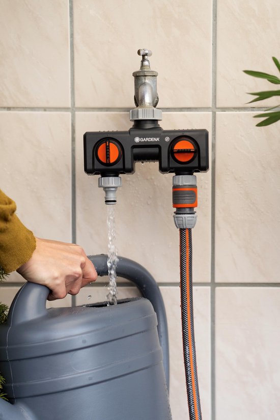 Gardena waterverdeler met twee oranje knoppen. Een slang is aangesloten, de ander vult een grijze gieter.