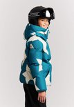 Meisje in blauwe winterjas met sterrenprint, van de zijkant gezien, met skihelm.