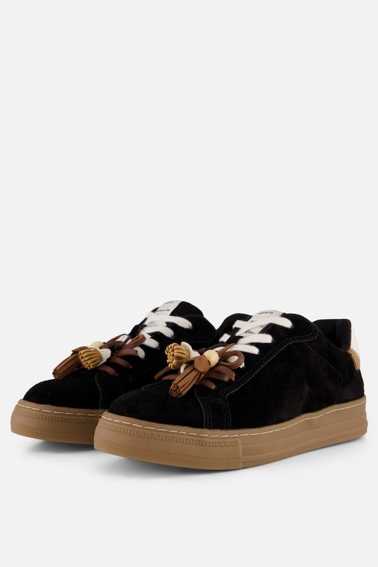 Twee zwarte suède sneakers met bruine zolen, witte veters en decoratieve kwastjes aan de voorkant.