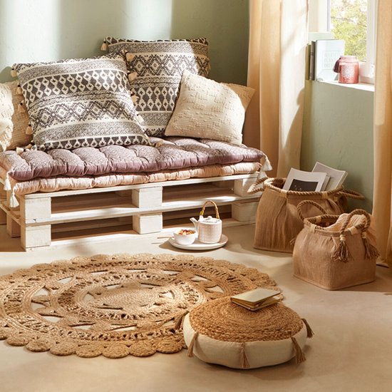 Pouf rond en beige en jute avec des franges décoratives et un petit livre posé dessus.