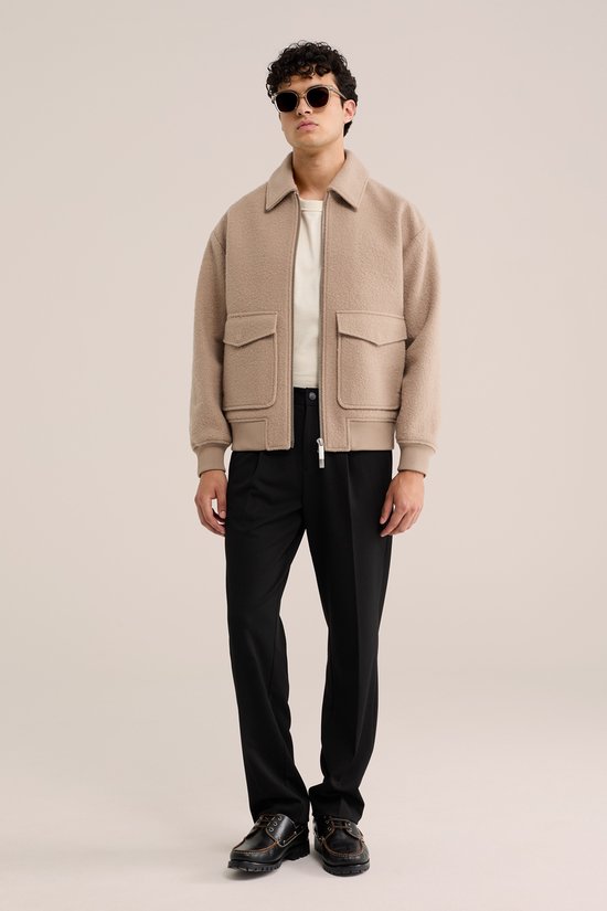 Man met zwarte pantalon, beige jas en witte top.
