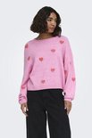 Model draagt roze trui met rode hartjesprint, lange mouwen en ronde hals.