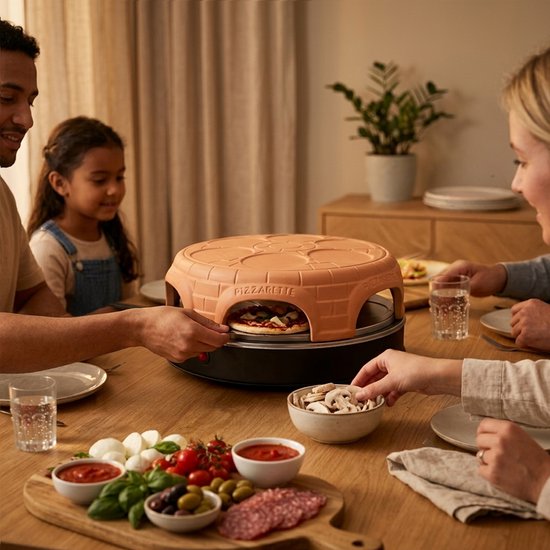 Een familie maakt pizza's rond de terracotta Pizzarette pizzaoven met ingrediënten.