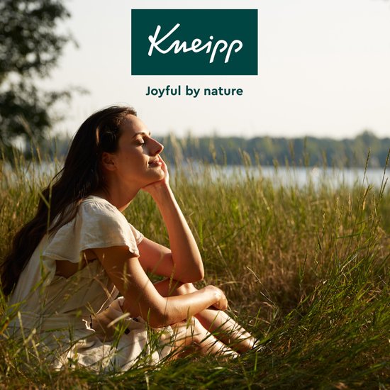 Vrouw ontspant in het gras met de ogen dicht, met een blije glimlach. Kneipp logo.