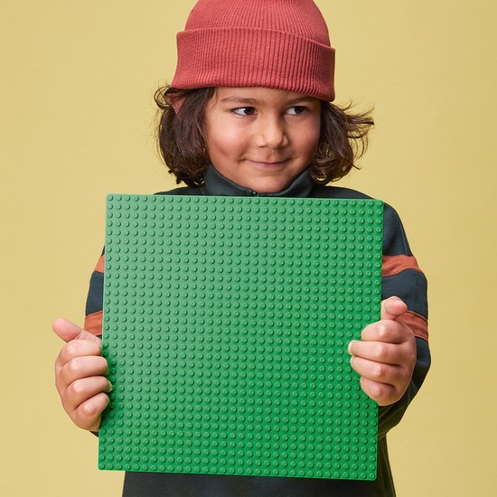 Jongen met rode muts houdt een groene LEGO bouwplaat met 10x10 noppen vast.