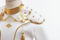 Gedetailleerde close-up van de gouden kraag en schouderdetails met bloemen en kwastjes op de witte top.
