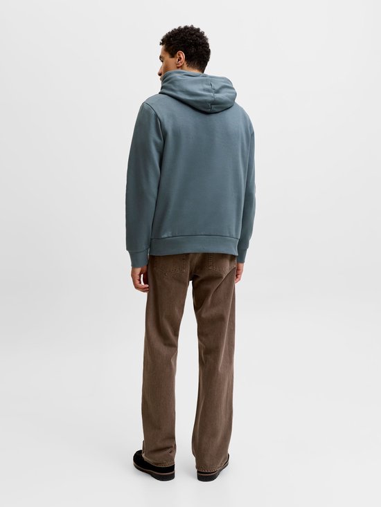 Man van achteren gezien, draagt een blauwgrijze hoodie en bruine broek.