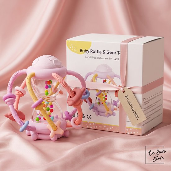 Roze zandloper rammelaar en bijtring, naast een cadeaubox op een roze satijnen doek.