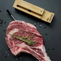 Meater+ thermometer in houten houder naast rauwe steak met tijm, peper en zout.