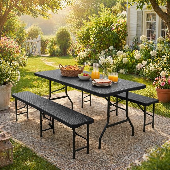 Zwarte, inklapbare picknicktafel met bankjes, gedekt met brood en sap in een tuin met bloemen.
