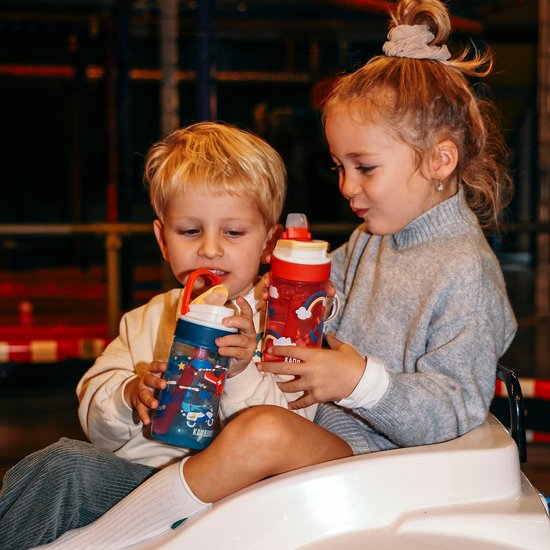 Jongen en meisje zitten met Kambukka drinkflessen. Meisje heeft een rode fles met vogels, jongen een blauwe met sterren.