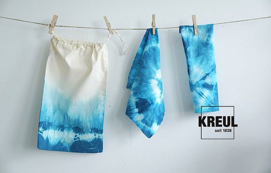 Trois pièces de tissu à imprimé batik bleu sèchent sur une corde à linge.