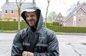 Man met op zijn fiets, draagt een zwarte regenjas met capuchon en reflecterende strepen. De jas heeft "VOLTANO" logo.