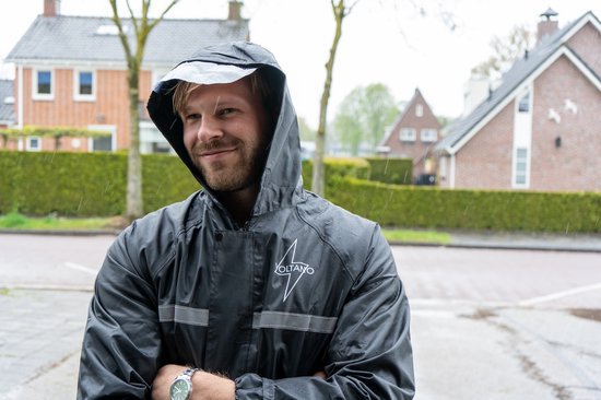 Man met op zijn fiets, draagt een zwarte regenjas met capuchon en reflecterende strepen. De jas heeft "VOLTANO" logo.