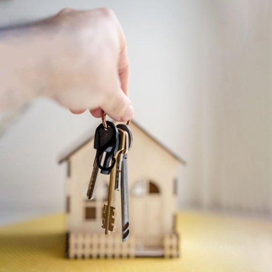 Hand houdt sleutels boven een miniatuur houten huis.