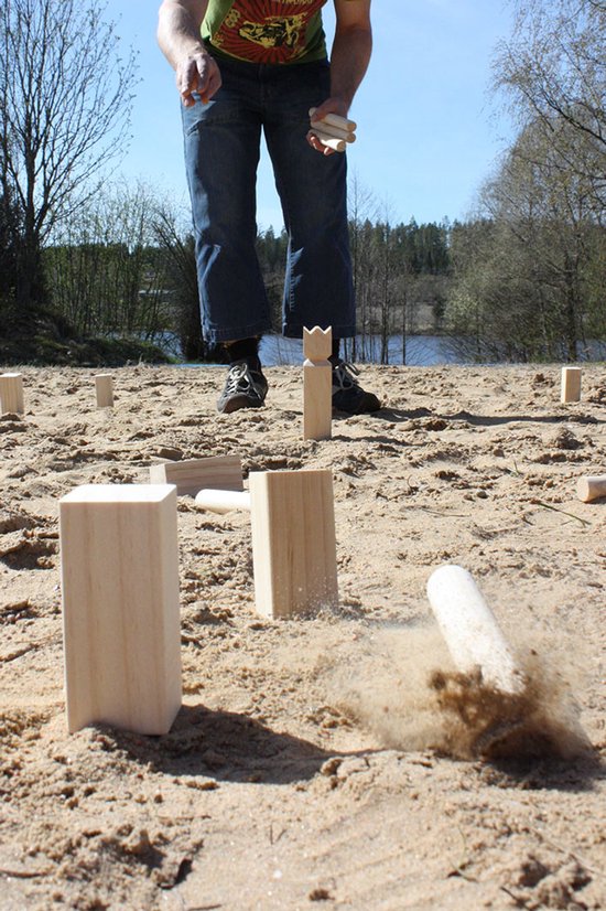 Een man gooit een werpstok naar houten Kubb skittles op een zanderige ondergrond.