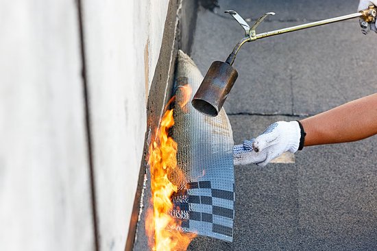 Hand met witte handschoen gebruikt brander met vlammen op dakbedekking.