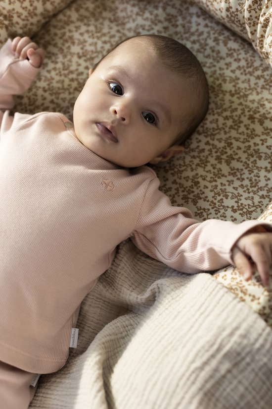 Baby in een roze longsleeve shirtje in een wiegje met bloemenprint