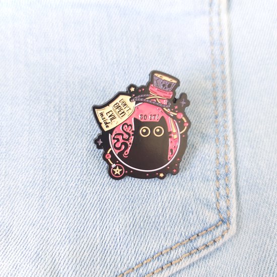 Emotionele pin met een zwarte kat in een fles met de tekst 'DO IT!' en 'DON'T OPEN EVIL inside', bevestigd aan een spijkerbroekzak.