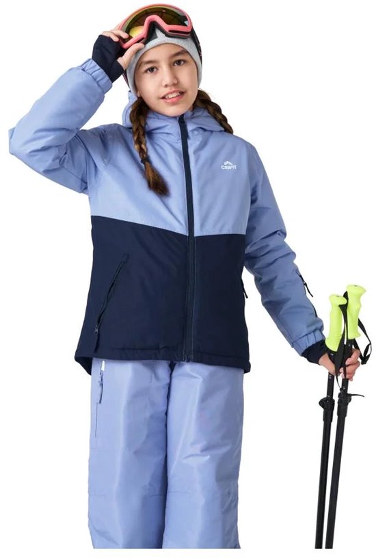 Meisje met gevlochten haar draagt lichtblauwe en donkerblauwe ski jas, skibroek en skibril. Ze houdt skistokken vast.