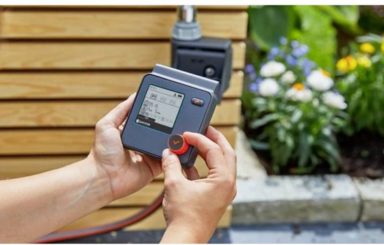 Handen die een Gardena besproeiingscomputer met digitaal display instellen.