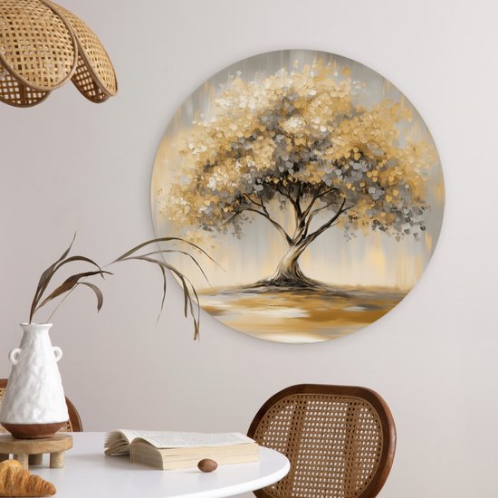 Ronde muurcirkel met een schilderij van een boom met gouden en grijze bladeren, in een woonkamer met een rotan stoel en bijzettafel.