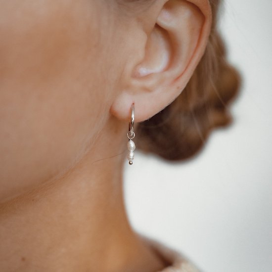 Close-up van een oor met een zilverkleurige oorring met twee hangende zoetwaterparels.