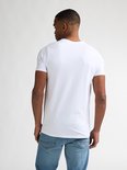 Man met korte zwarte haren, met baardje, draagt een wit V-hals T-shirt, gezien van achteren.