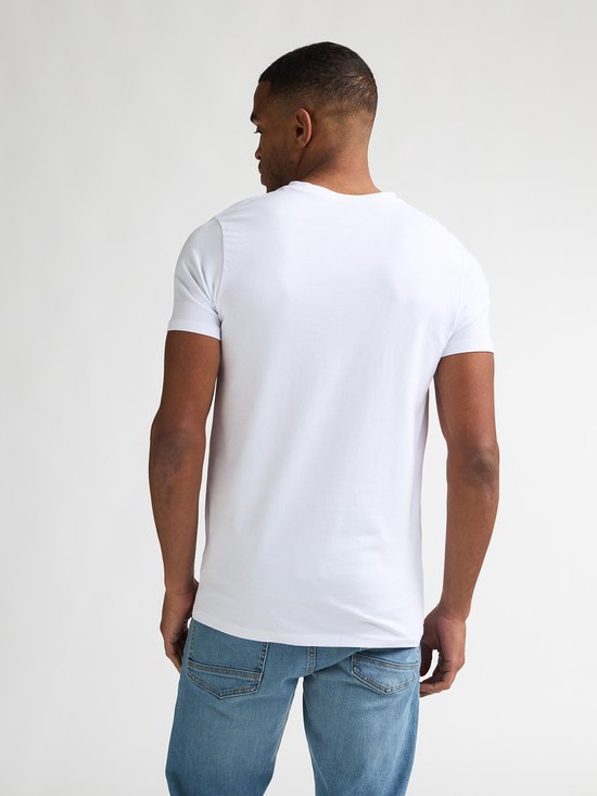 Man met korte zwarte haren, met baardje, draagt een wit V-hals T-shirt, gezien van achteren.