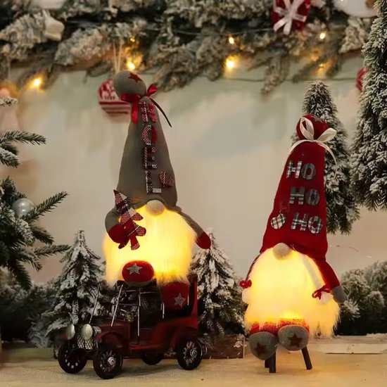 Twee verlichte kerstkabouters, één op een rode auto, met grijze en rode hoeden en witte baarden.