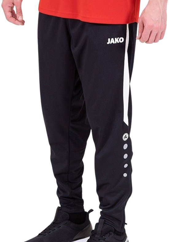 Zwarte Jako trainingsbroek met witte streep op de zijkant en drukknoopjes onderaan. Model met rode shirt.
